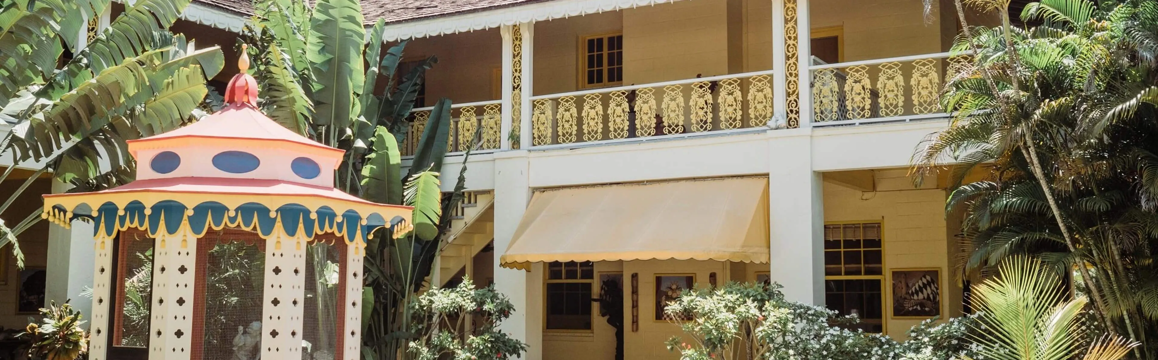 Courtyard at Bonnet House Museum & Gardens with the historic yellow estate, ornate wrought-iron balcony, and decorative gazebo among tropical plants