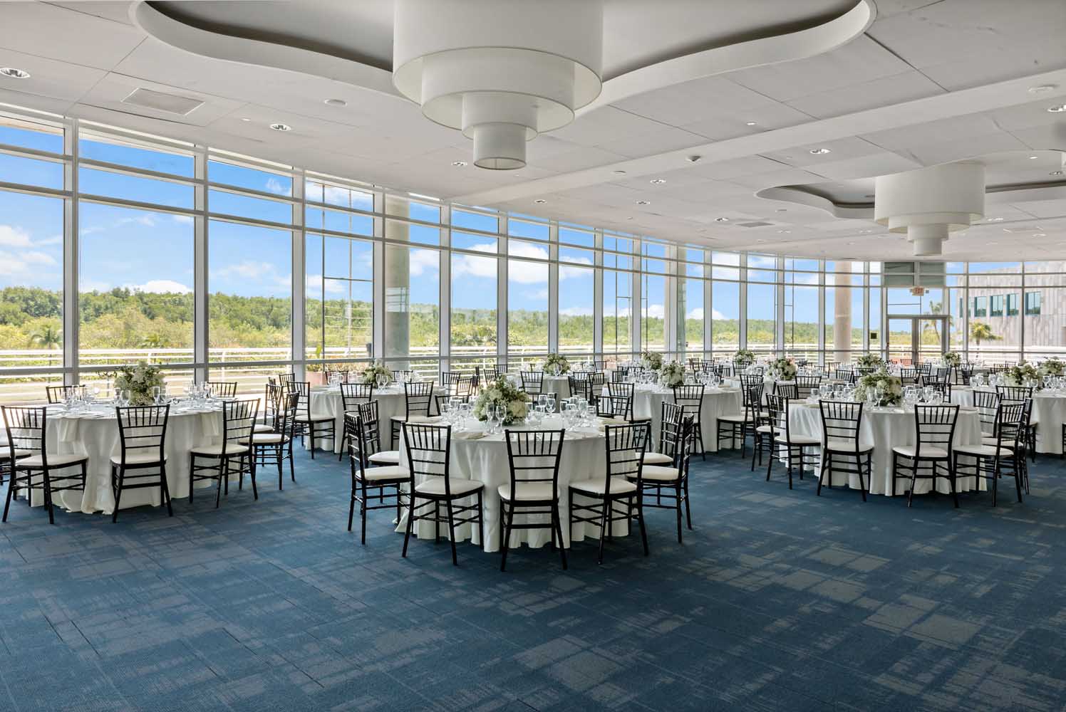 Palm Ballroom at Palmetto Bay Village Center set for a reception with round tables, white linens, and floor-to-ceiling windows overlooking tropical greenery
