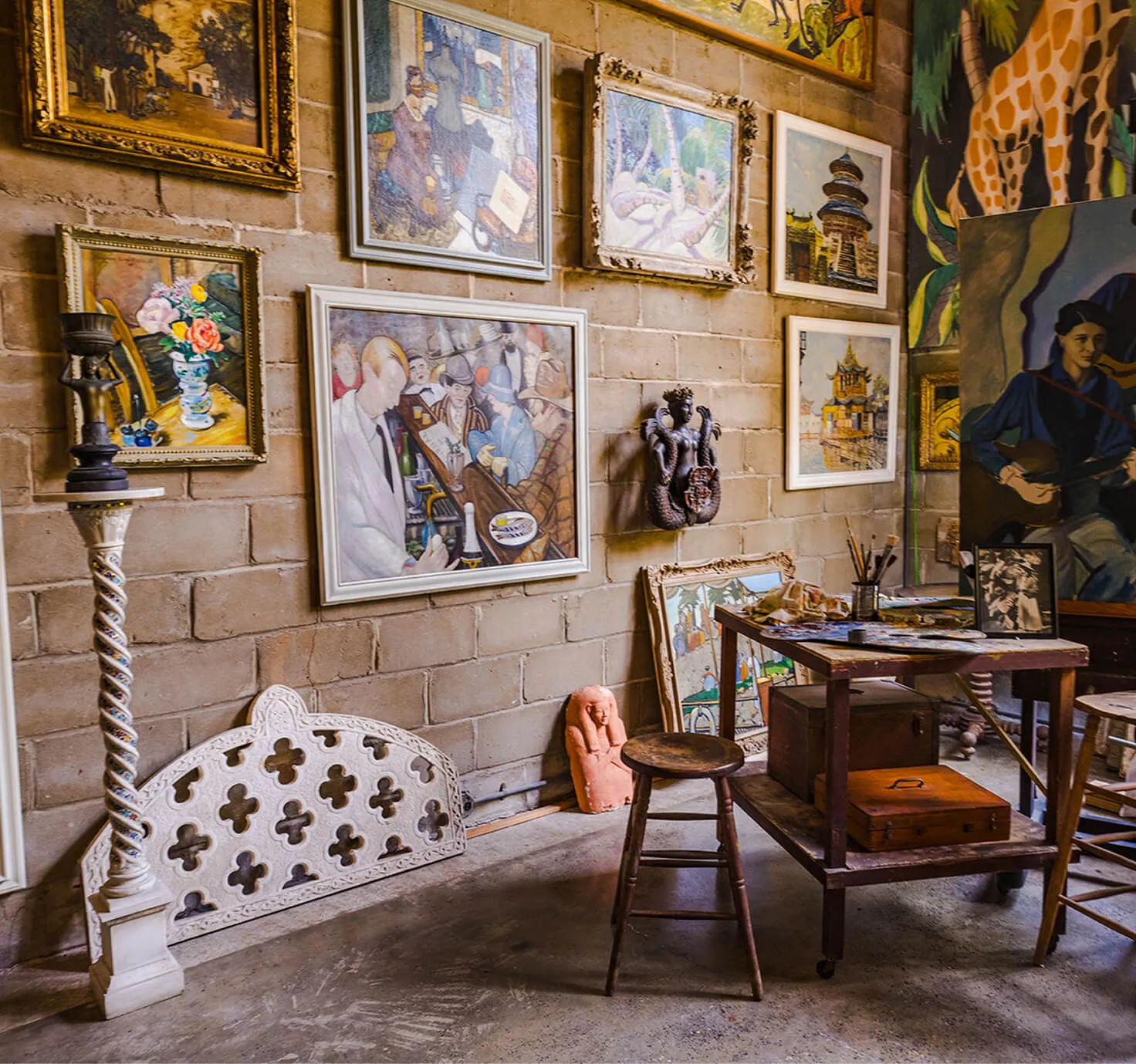 Artist studio interior at Bonnet House with framed paintings, a rolling workbench of palettes and brushes, and exposed stone walls