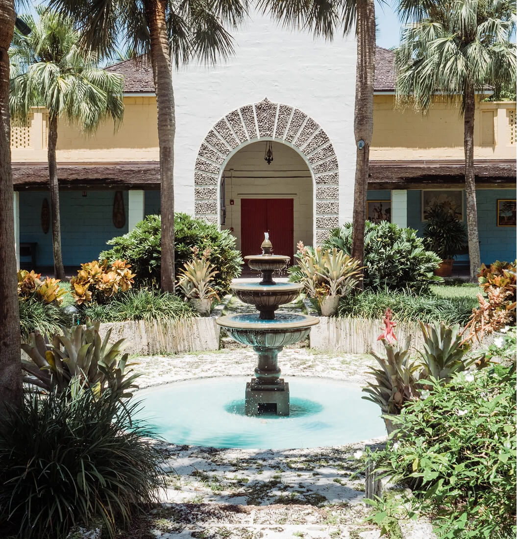 Courtyard fountain at Bonnet House framed by a shell-encrusted archway, red doors, and tropical landscaping