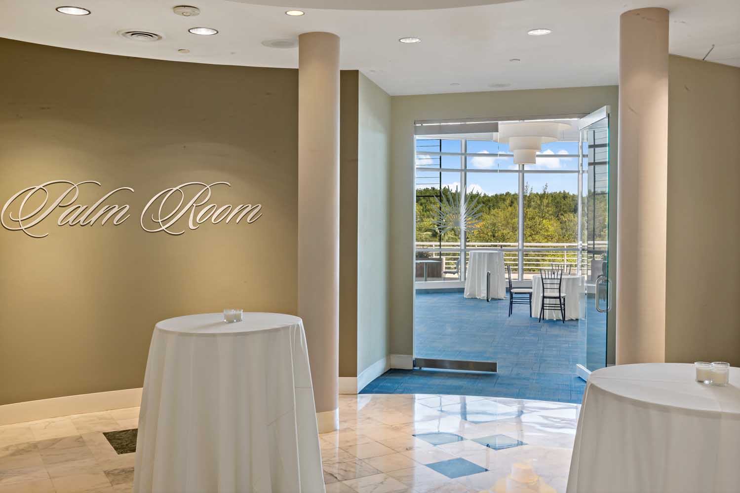 Palm Room pre-function area with cocktail tables opening to an outdoor terrace overlooking lush greenery