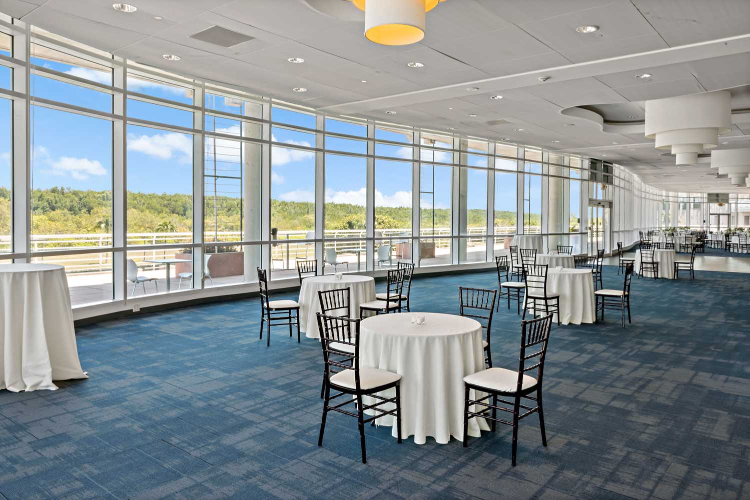 Bright ballroom at Palmetto Bay Village Center with floor-to-ceiling windows, white linens, and views of the surrounding forest