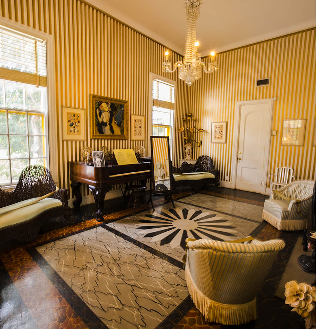 Striped yellow salon at Bonnet House with a crystal chandelier, grand piano, and inlaid sunburst floor