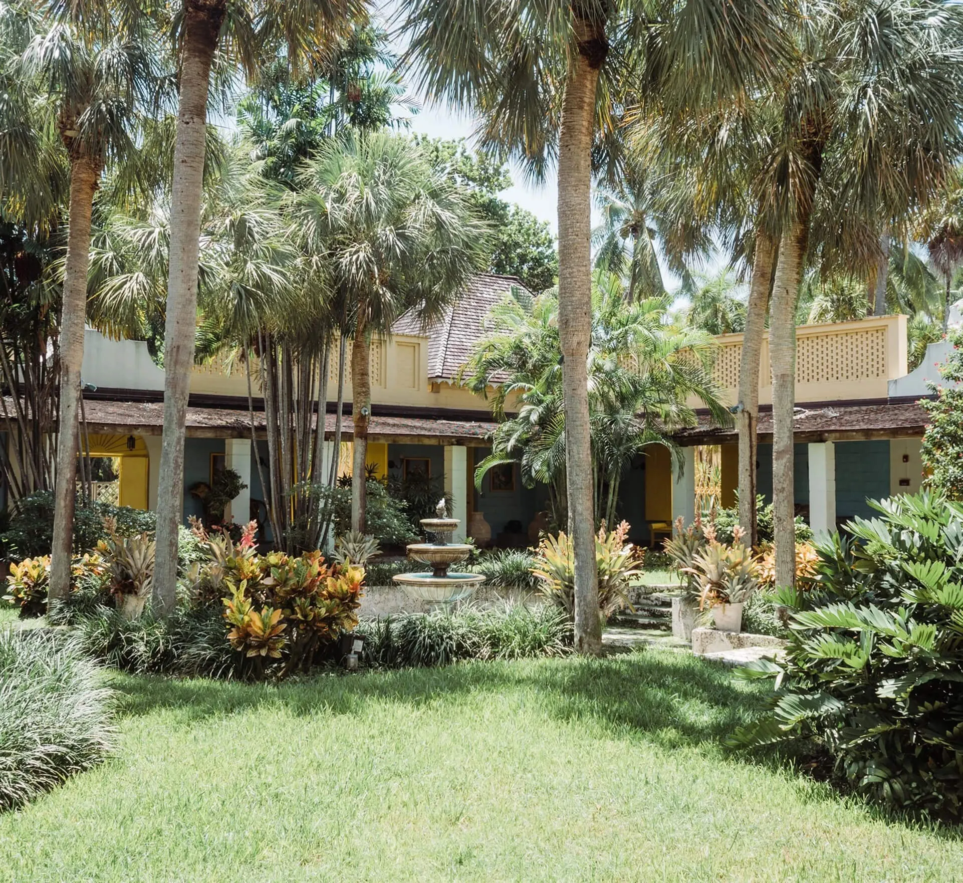Garden lawn at Bonnet House with a three-tiered fountain, royal palms, and the historic estate veranda