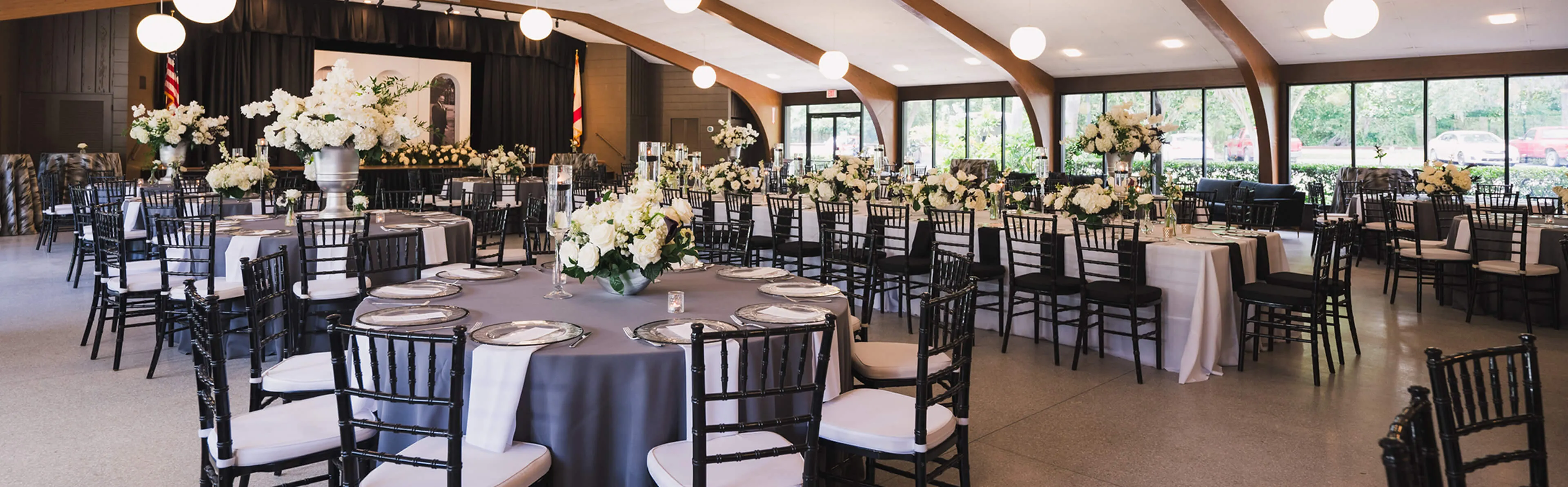 Indoor wedding reception at Venue on Lake Lily in Maitland with vaulted wood-beam ceiling, globe pendant lights, and round tables set with white floral centerpieces