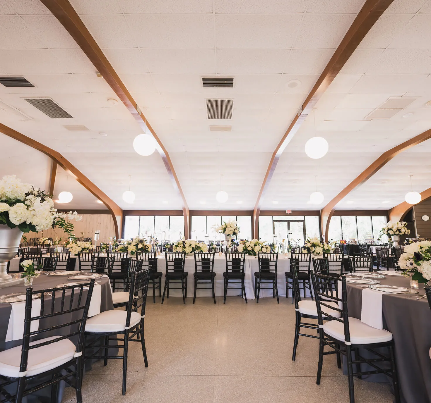 Spacious reception hall at Venue on Lake Lily in Maitland with grey round tables, white head table, Chiavari chairs, and floor-to-ceiling windows
