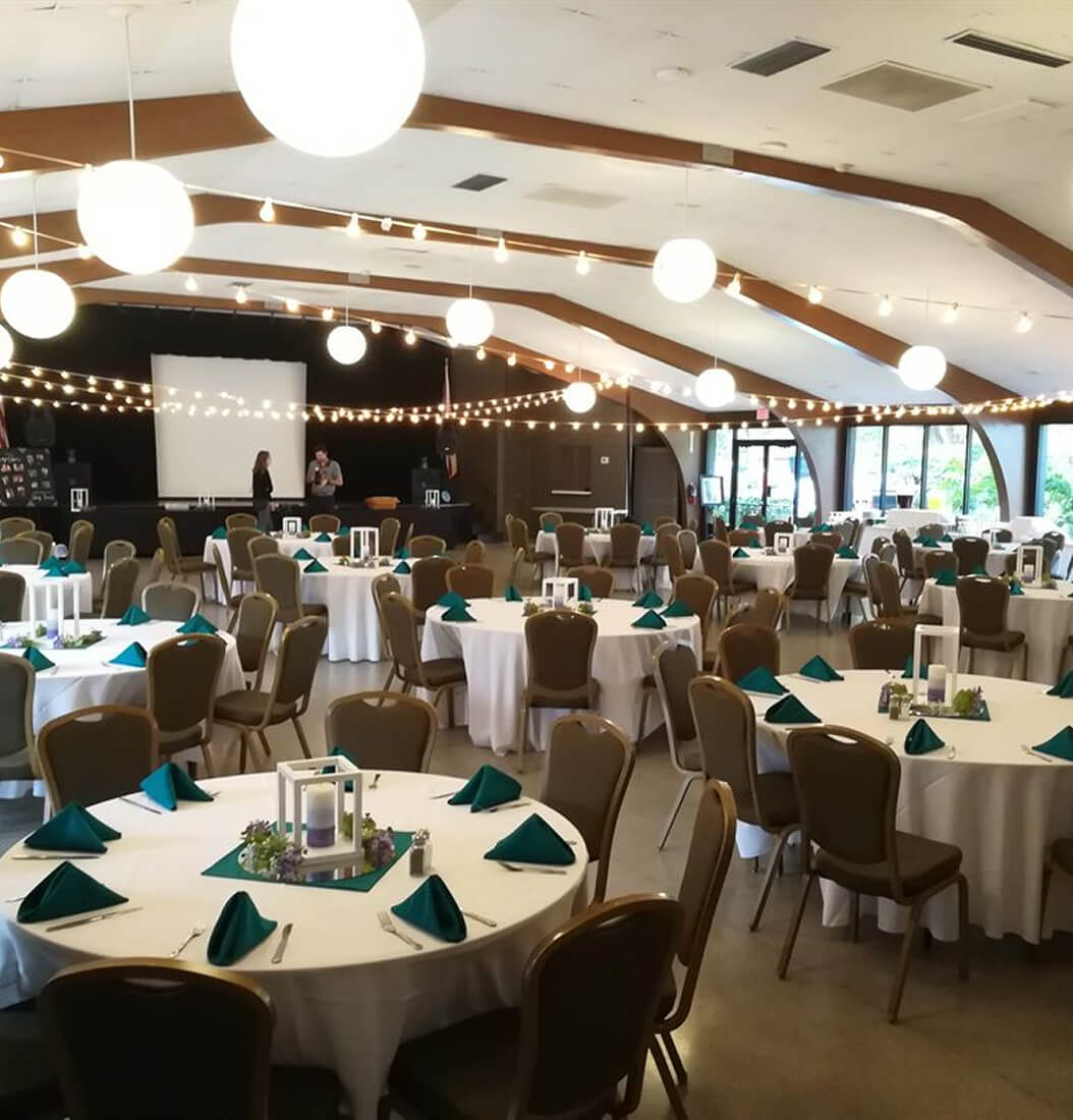 Banquet hall at Venue on Lake Lily in Maitland with white round tables, teal napkins, lantern centerpieces, string lights, and elevated stage