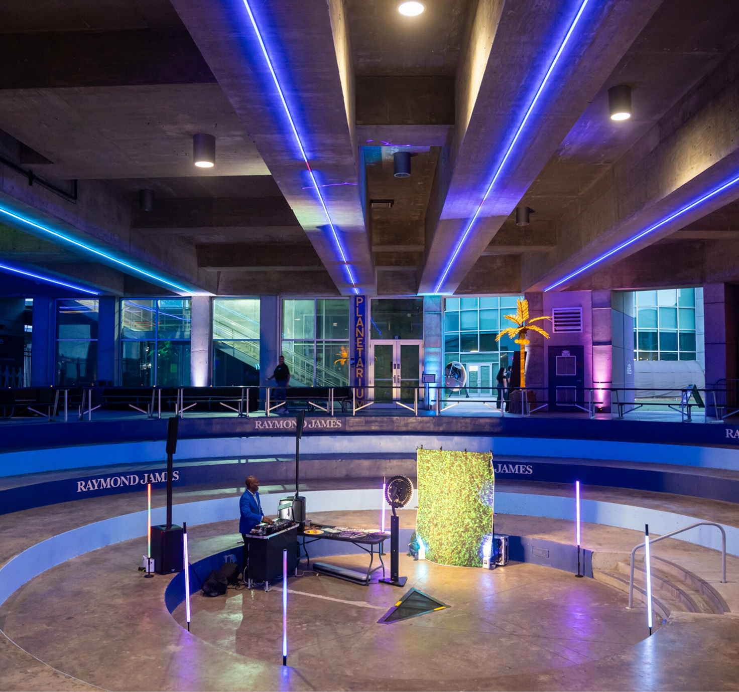 Circular amphitheater event space at MOSI with blue tiered seating, neon lighting, and DJ setup near the planetarium