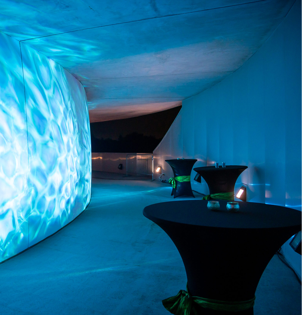 Cocktail high-top tables along a curved blue-lit corridor at MOSI