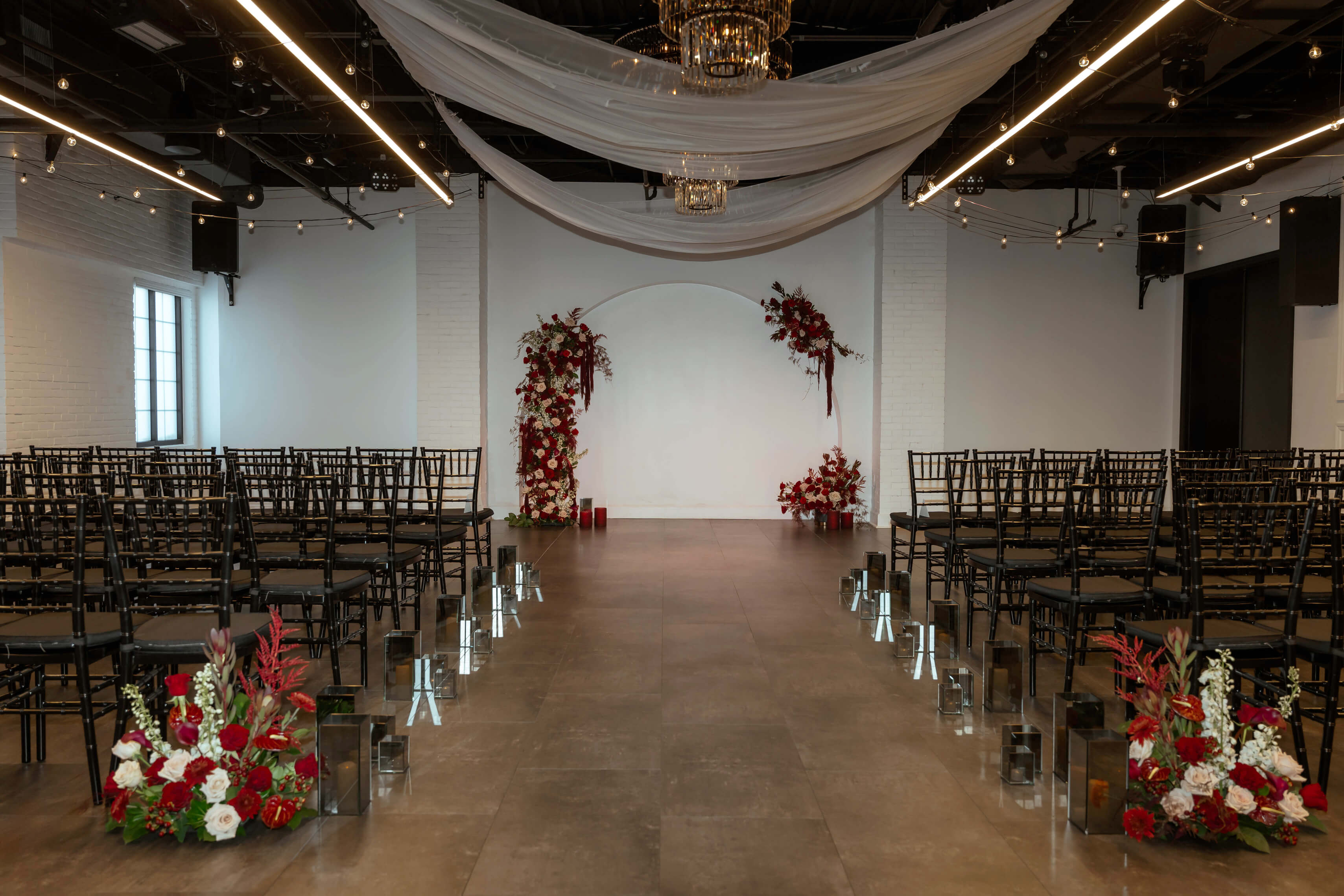 Elegant reception hall with draped ceilings, brick walls, string lights, and floral centerpieces at Trellis 925