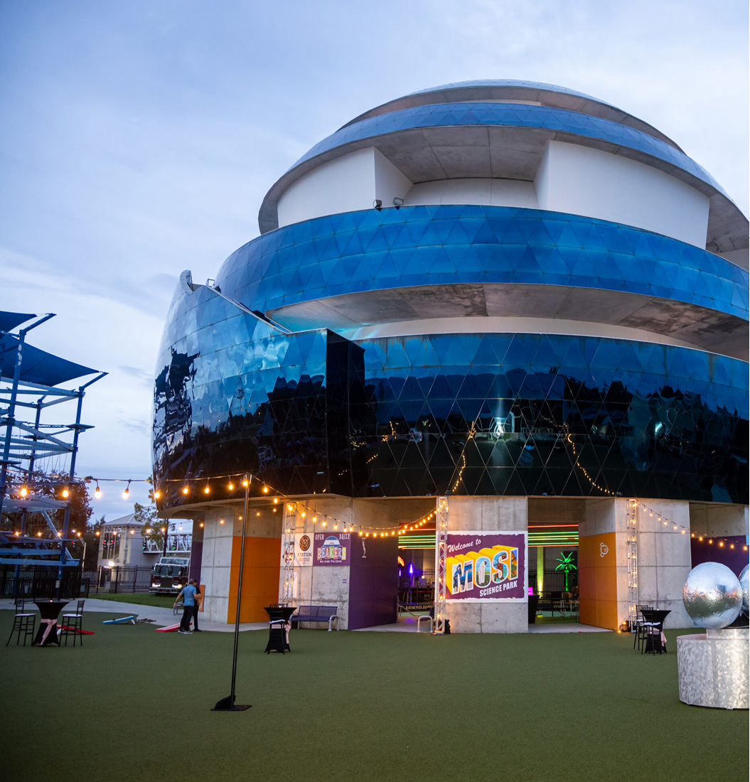 Evening outdoor event at MOSI Science Park with string lights, cocktail tables, and the blue geometric dome facade