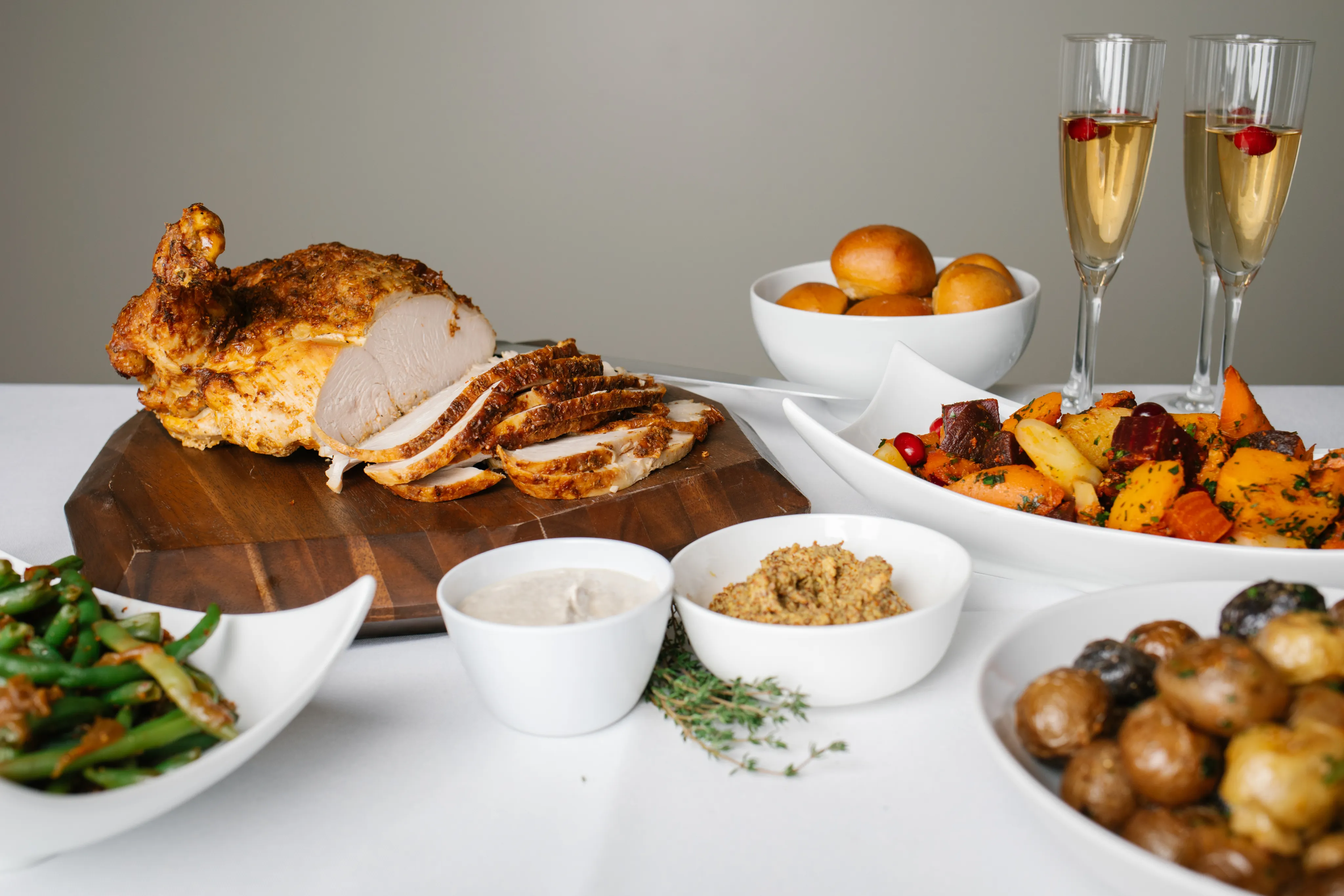 Carved roast turkey on a wooden board with roasted root vegetables, dinner rolls and sides