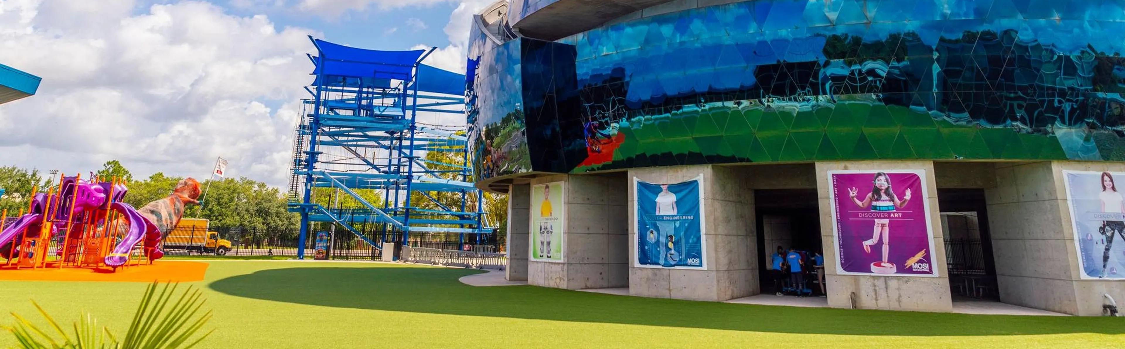 Exterior of MOSI Museum of Science & Innovation in Tampa with modern blue geometric facade, outdoor playground, and ropes course