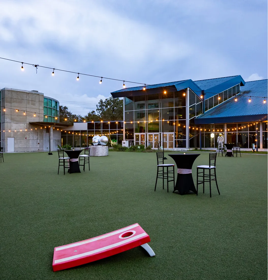 Outdoor cocktail reception at MOSI with high-top tables, string lights, and the museum’s modern glass facade at dusk