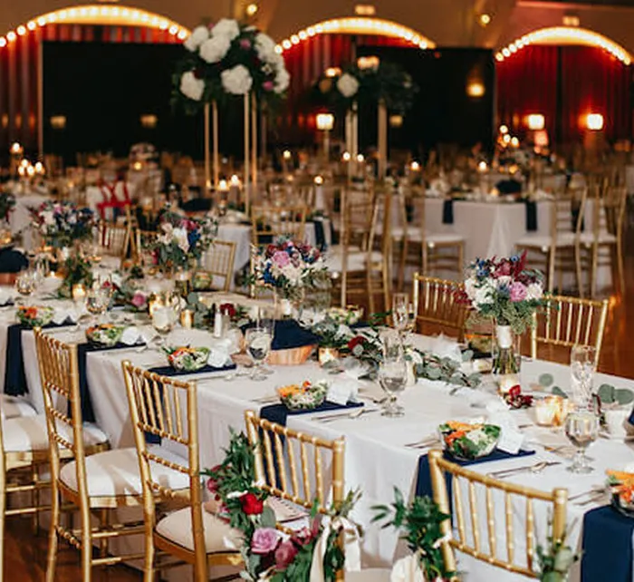 Historic Coliseum event venue exterior with white stucco walls, arched windows and tropical palm trees under clear sky