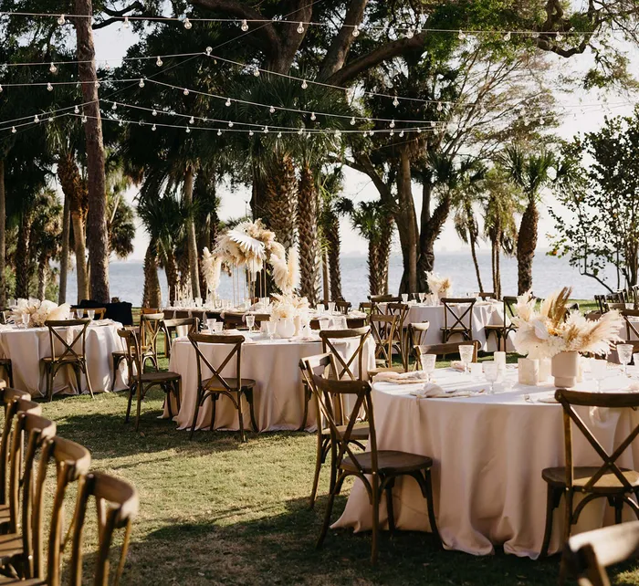 Outdoor wedding venue at Powel Crosley Estate with couple, round tables, wooden chairs, and string lights